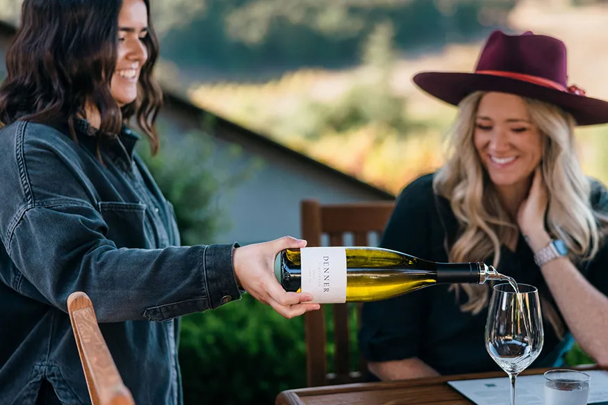 Denner winery staff pouring white wine for a guest wear a wide brim hat.